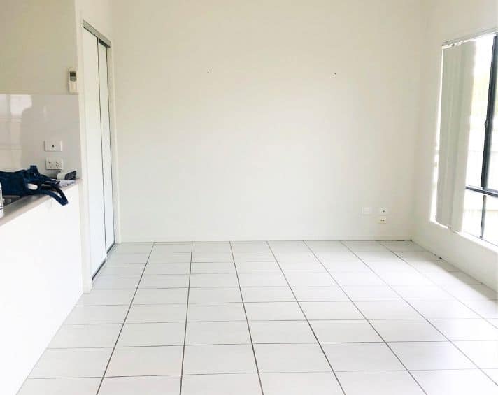 Empty room with white tiled floor, white walls, a sliding door wardrobe, and large windows on the right letting in natural light.