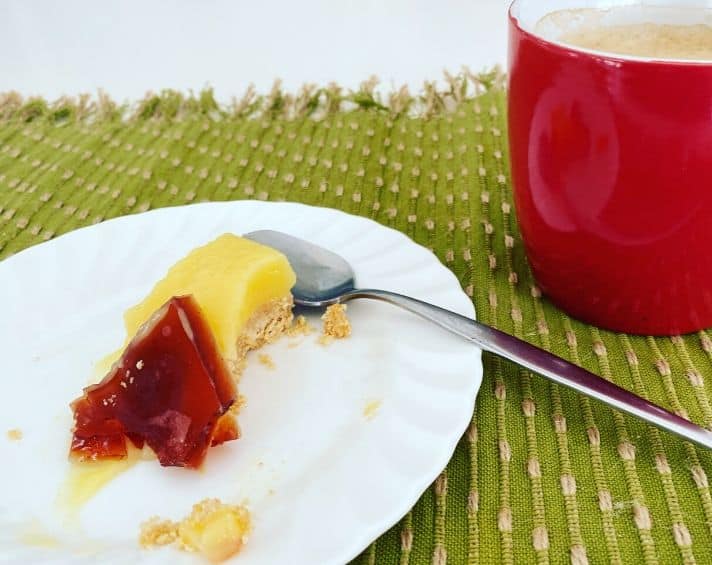 A slice of caramel-topped pudding on a white plate with a spoon, next to a red mug on a green placemat.