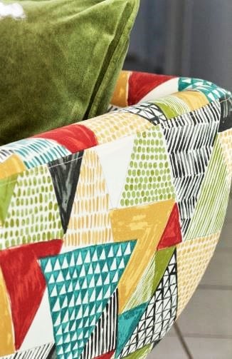 Close-up of a chair with a colourful, geometric-patterned fabric and a green cushion on the seat.