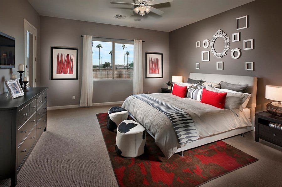 Modern bedroom with a large bed, red and grey accents, two bedside tables, a chest of drawers, wall art, and a window with a view of palm trees.