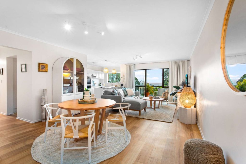 Open-plan living and dining area with wooden floors, round dining table, cosy sofa, large window, and neutral décor with natural light.