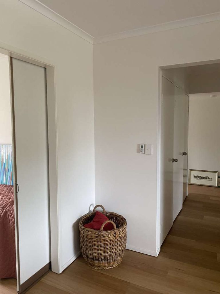 A wicker basket with red towels sits on a wooden floor near a white wall, adjacent to sliding wardrobe doors and a hallway with closed doors.