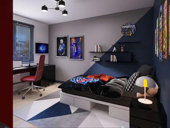 Modern bedroom with a bed, angular rug, desk with computer, red chair, wall art, shelves, and decorative items. Natural light enters through window blinds on the left.