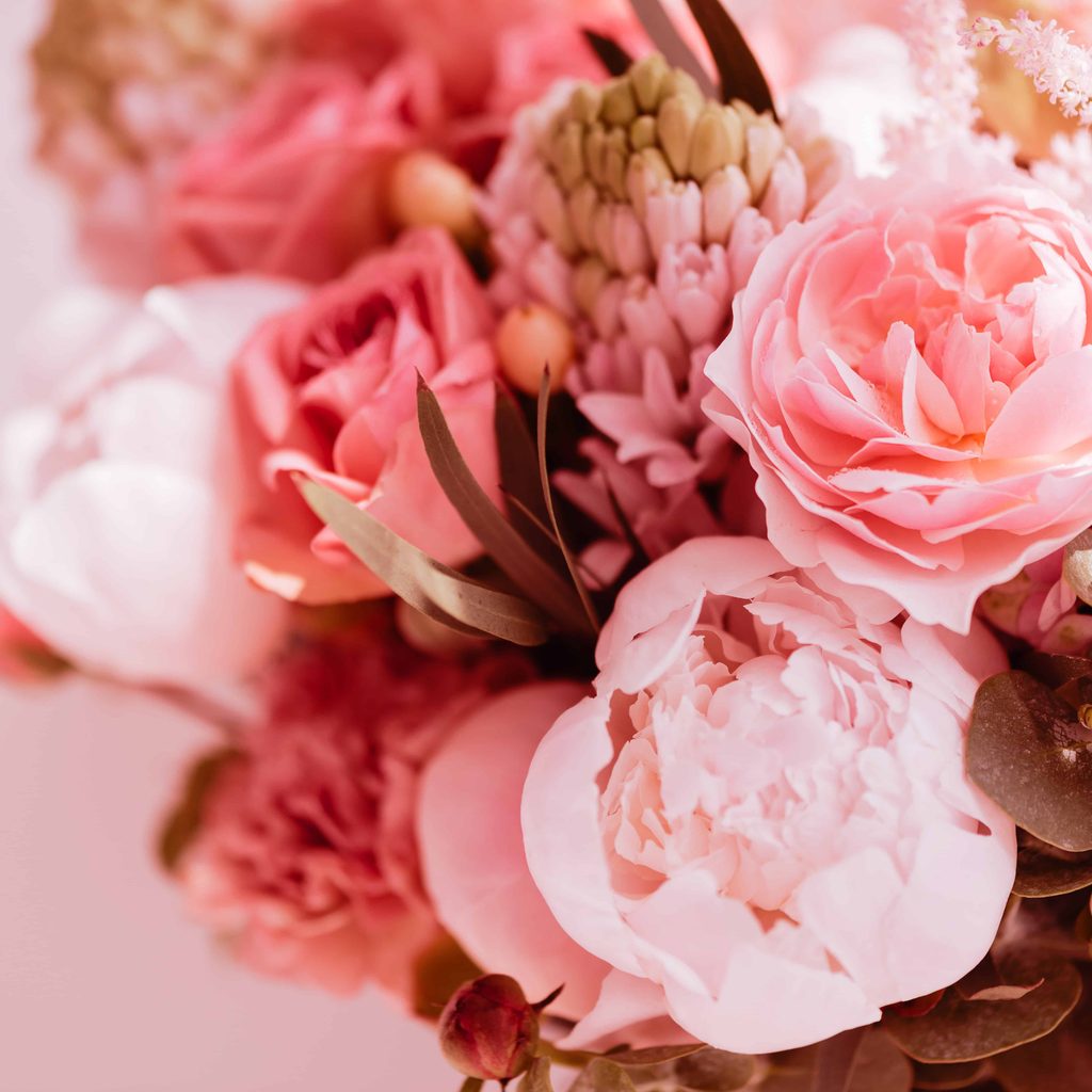 A close-up of a bouquet featuring pink and white peonies, roses, and assorted greenery with soft lighting.