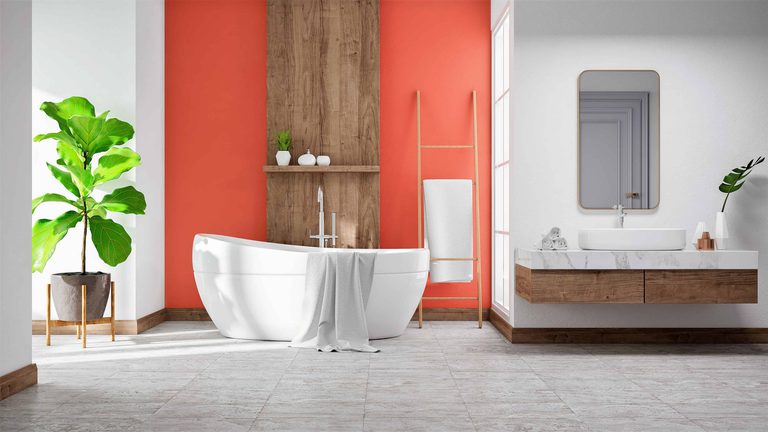 Modern bathroom with a white freestanding bath, wooden accents, a potted plant, orange feature wall, floating vanity unit, and a rectangular mirror. A towel hangs on a wooden ladder by the bath.