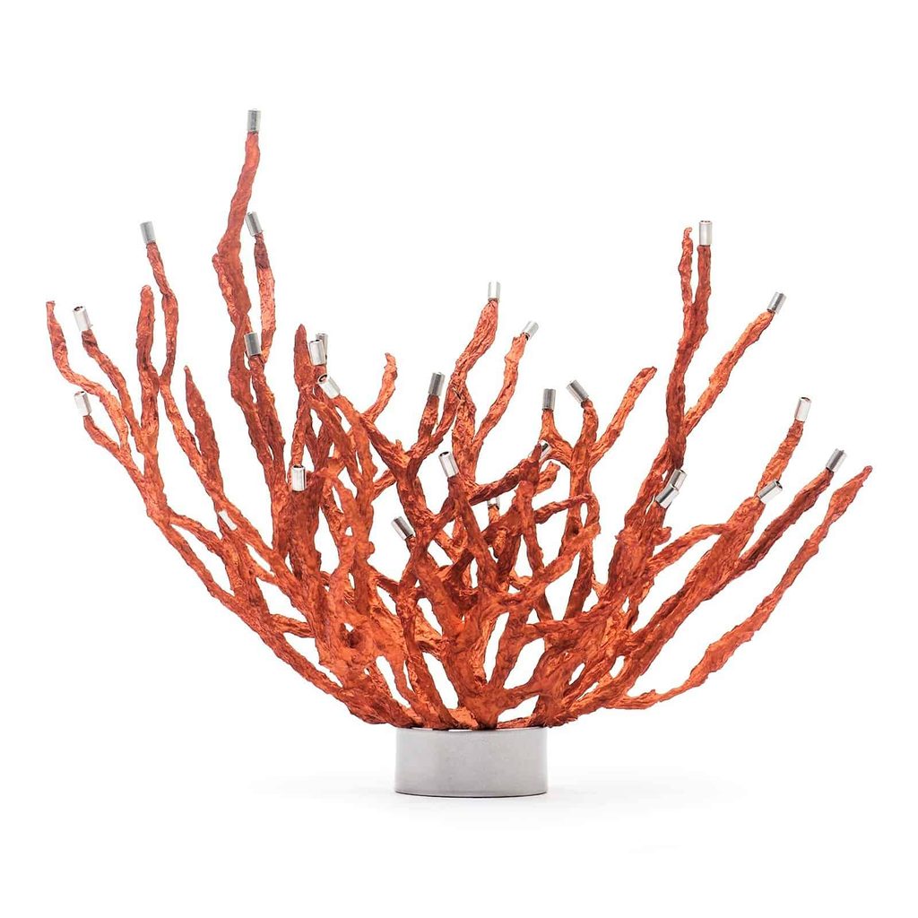 A red, branching sculpture with metal tips on each branch extends upward from a round silver base.