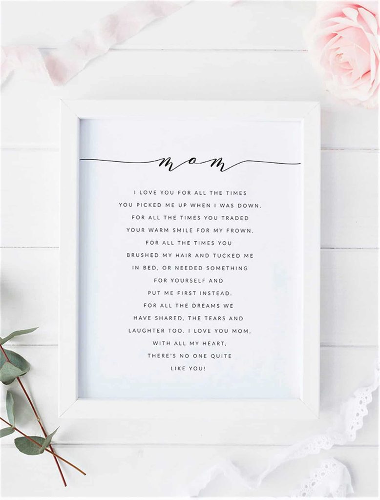 A framed poem titled “Mum” placed on a white surface, surrounded by pink roses, ribbon, and green leaves, expressing love and gratitude to a mother.