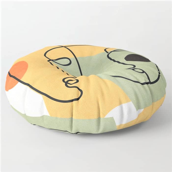 Round cushion with an abstract design in green, yellow, white, orange, and black, featuring curved and circular shapes.