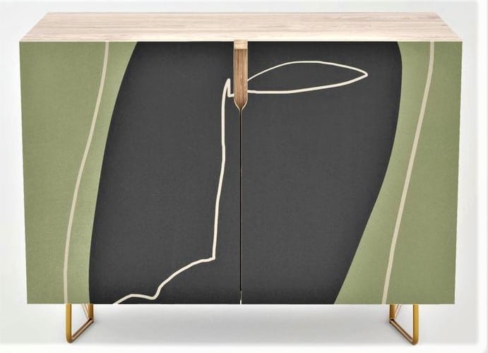 A modern cupboard with abstract green, black, and beige design on the front and gold legs.