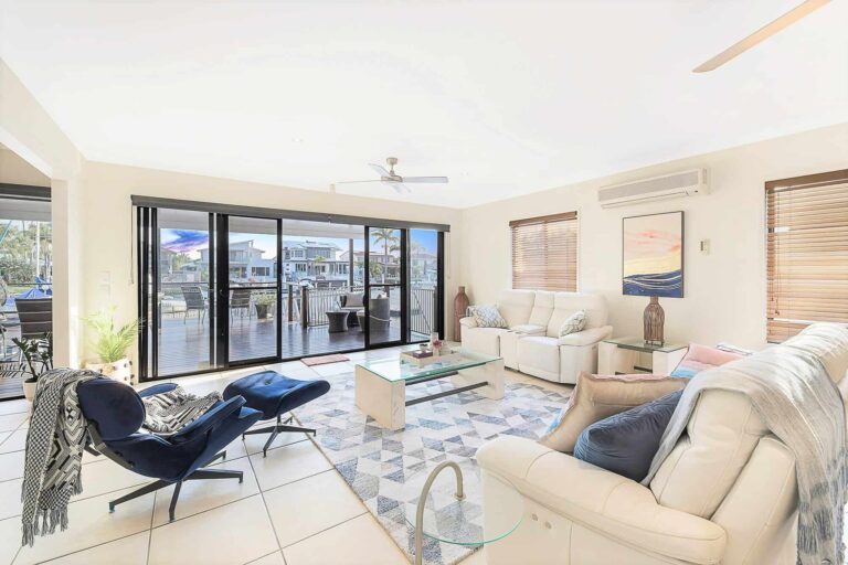 Bright living room with modern furniture, large sliding glass doors opening to a decking, geometric rug, and artwork on the walls.