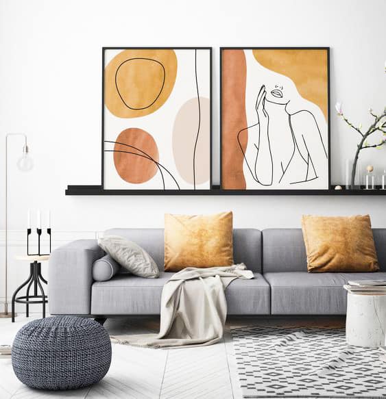 Modern living room with a grey sofa, gold cushions, a grey pouffe, abstract art on the wall, and minimalist decor including candles and a small flower arrangement.
