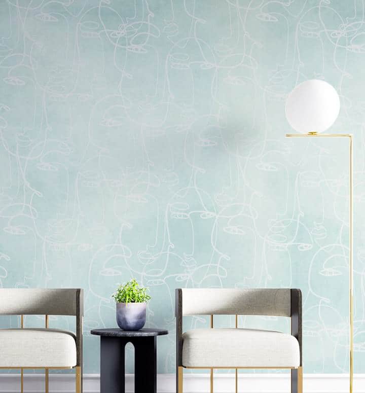Two modern chairs and a small table with a plant sit in front of a pale blue wall with abstract white line art, alongside a tall standard lamp with a round white shade.