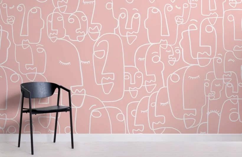 A black chair sits in front of a pink wall decorated with abstract white line drawings of faces.