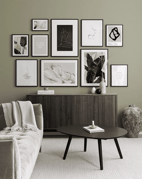 Neutral-toned living room with a beige sofa, round black coffee table, large vase, and a gallery wall of minimalist framed art above a wooden sideboard.