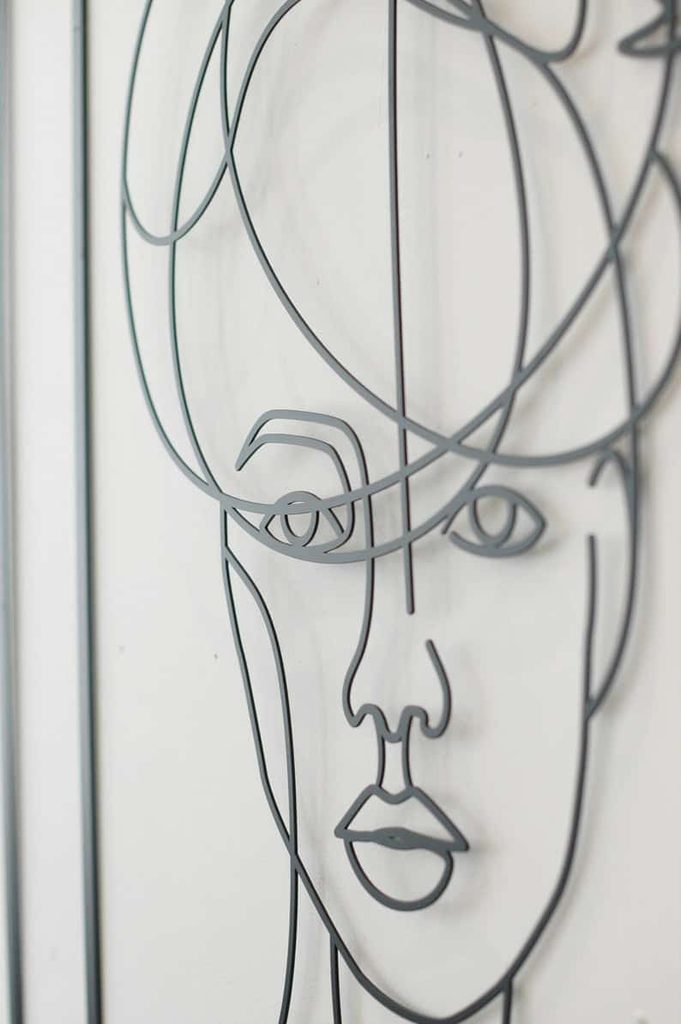 Black wire wall sculpture depicting an abstract human face with minimal, continuous lines on a white background.
