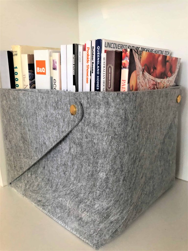 Grey felt box holding assorted books and magazines, positioned on a white shelf.