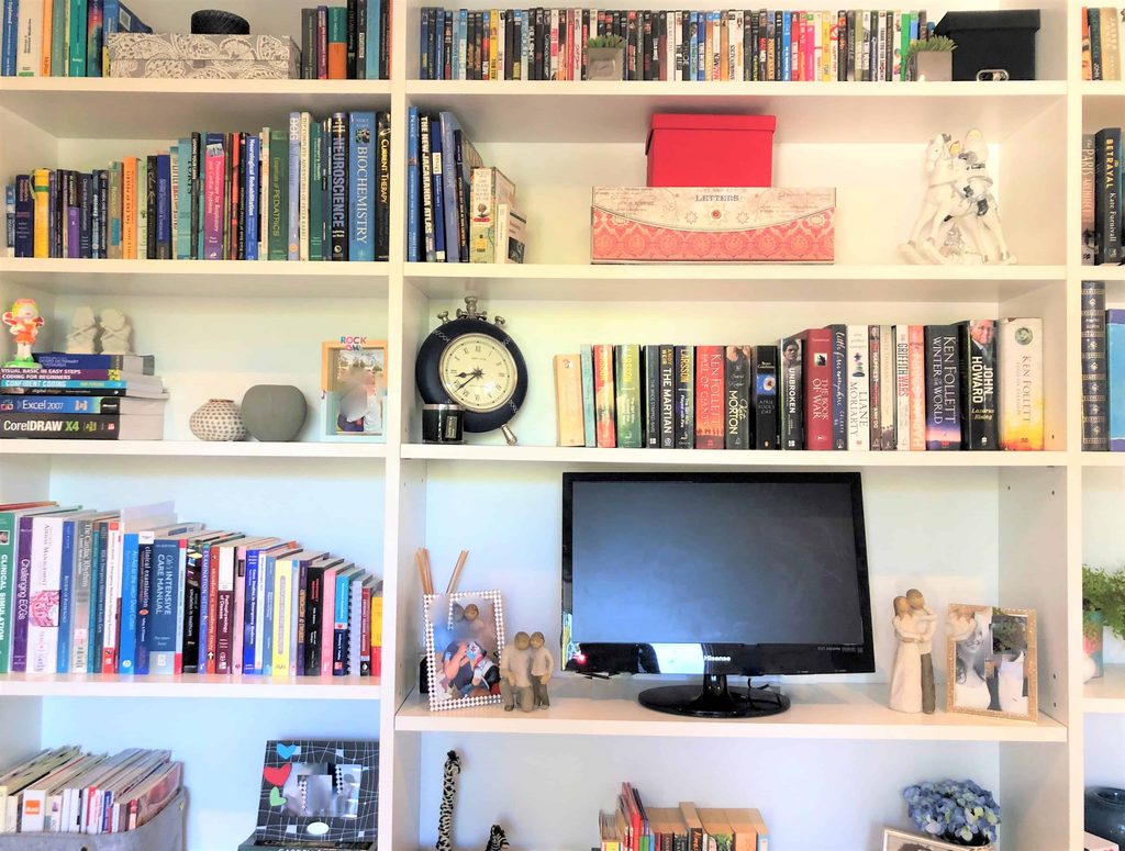 White bookcase filled with books, decorative items, a small clock, framed photos, and a flat-screen monitor in the centre.
