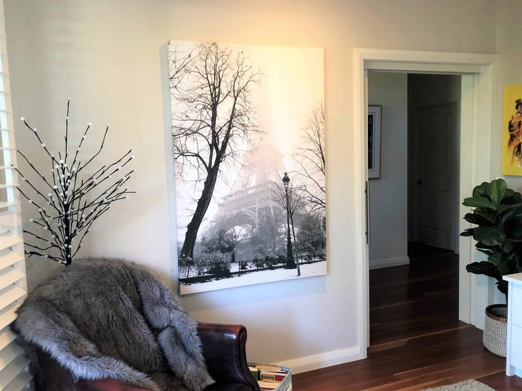 A living room corner with a leather armchair, fur throw, potted plant, and a black-and-white wall art of the Eiffel Tower.