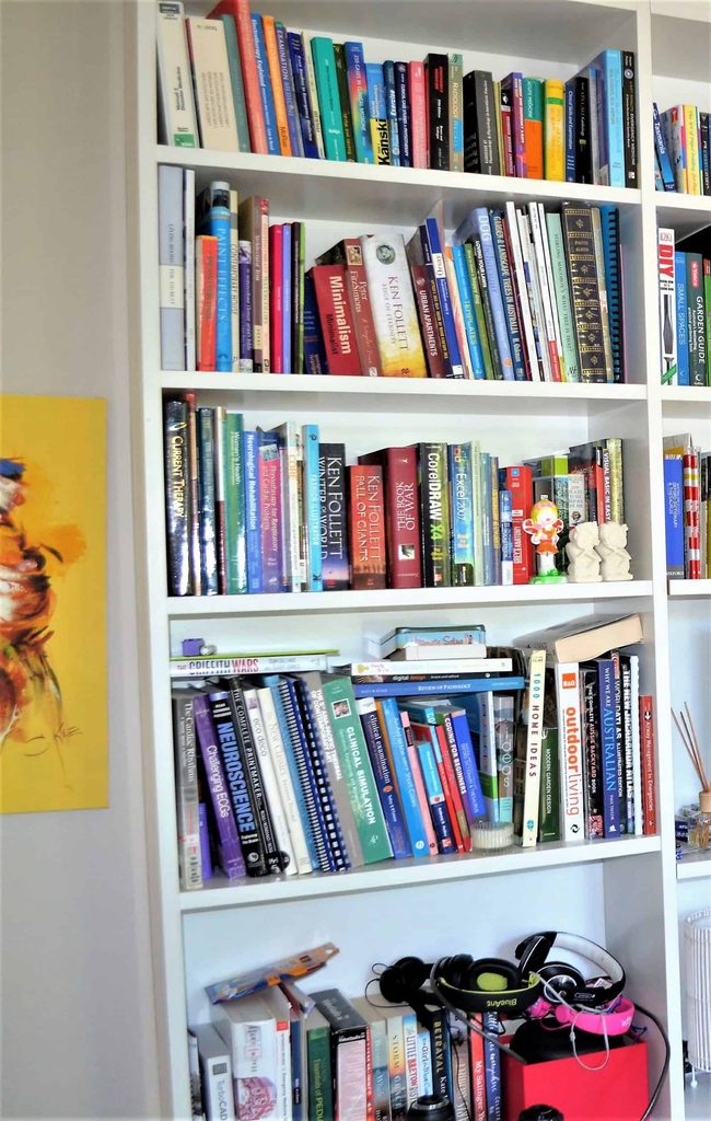 A white bookcase filled with various books, some stacked vertically and horizontally, along with headphones and small objects on the bottom shelf.