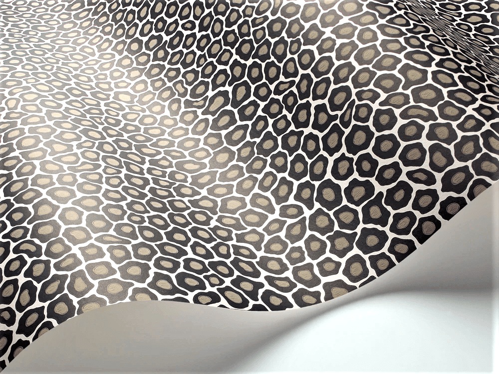 A sheet of paper with a repeating pattern of irregular black and beige spots, resembling an abstract animal print, lies partially curled on a white surface.