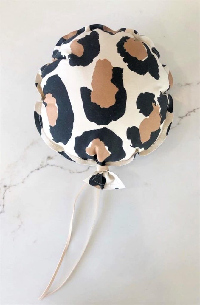 A round balloon with a leopard print pattern and a light ribbon attached, placed on a white marble surface.