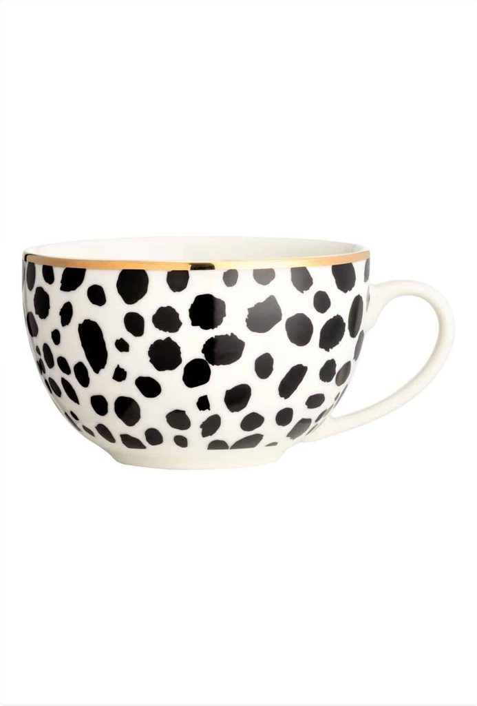 A white ceramic mug with black irregular spots and a gold rim, featuring a single handle on the right side.