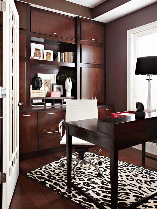 Modern home office with dark wood shelves, white chair, desk, window, lamp, and a black and white animal print rug on the floor.