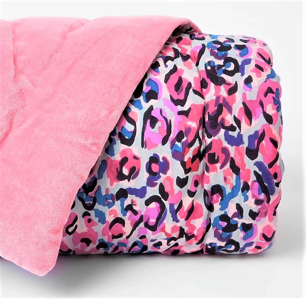 A folded duvet with a pink top side and a colourful leopard print pattern in pink, blue, and black on the other side.