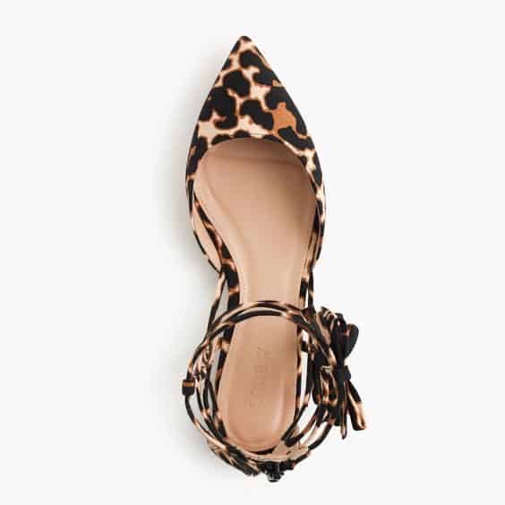 Leopard print pointed-toe flat shoe with ankle strap and bow, viewed from above on a white background.