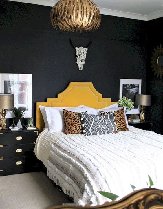 A bedroom with a yellow headboard, animal print pillows, black walls, gold pendant light, and a decorative skull above the bed.