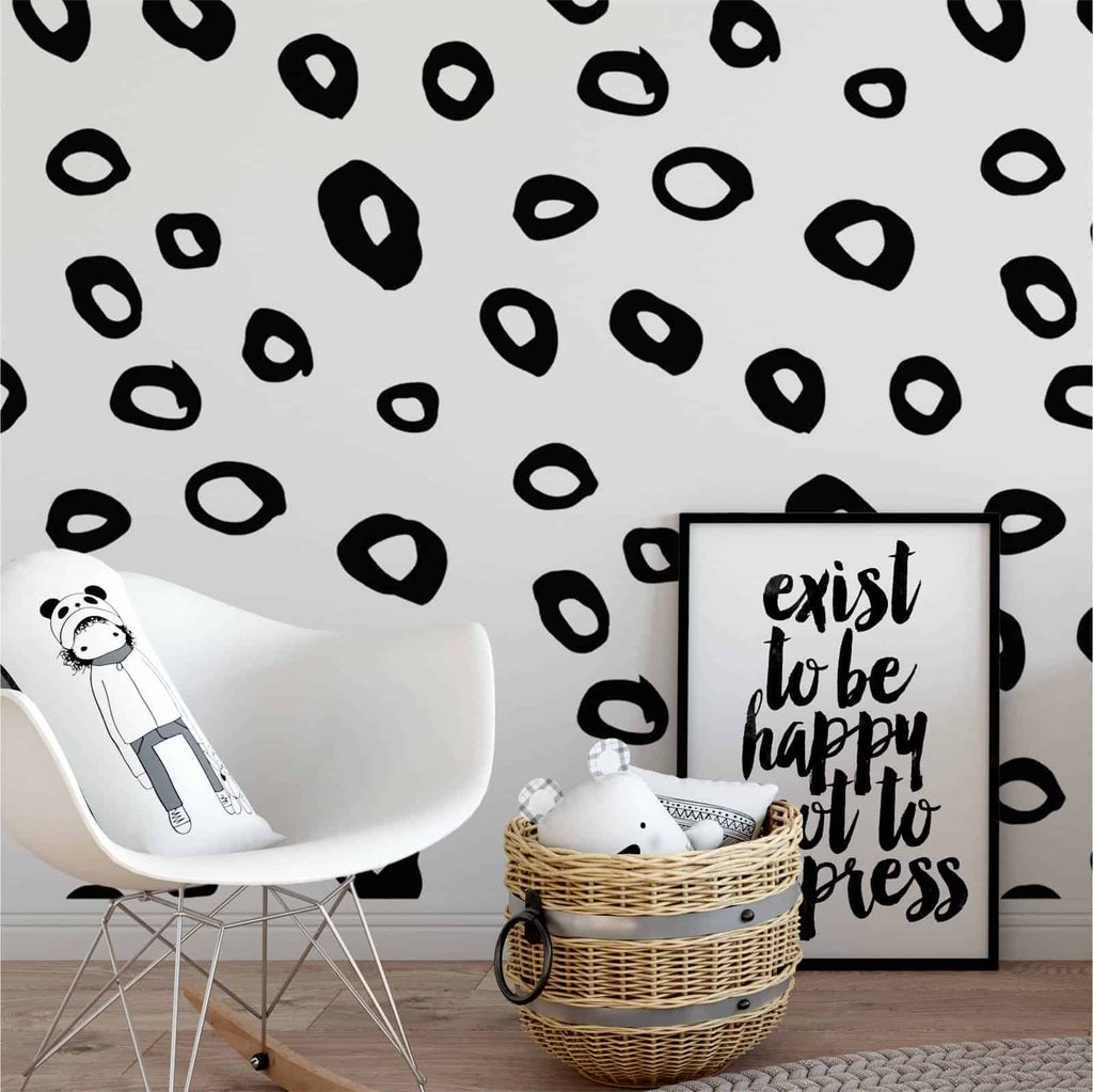 White room with black leopard print wall, a white chair with a bear cushion, a basket of soft toys, and a framed sign reading “exist to be happy not to impress.”.