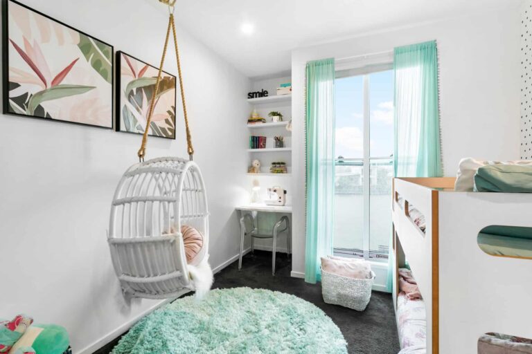 Bright kids’ bedroom with a hanging chair, bunk bed, small desk by the window, mint green curtains, round rug, and two botanical prints on the wall.